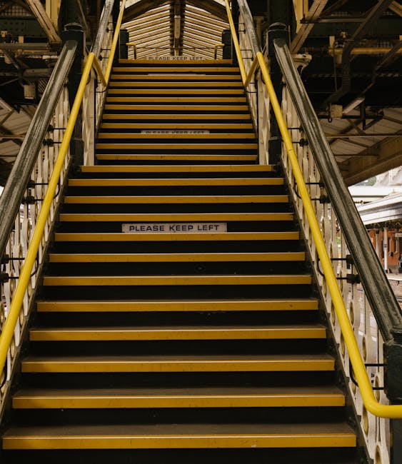 A set of industrial staircase and corridor lifts within a warehouse or loading facility, featuring yellow handrails on both sides and black and yellow striped treads. The stairs are constructed from m